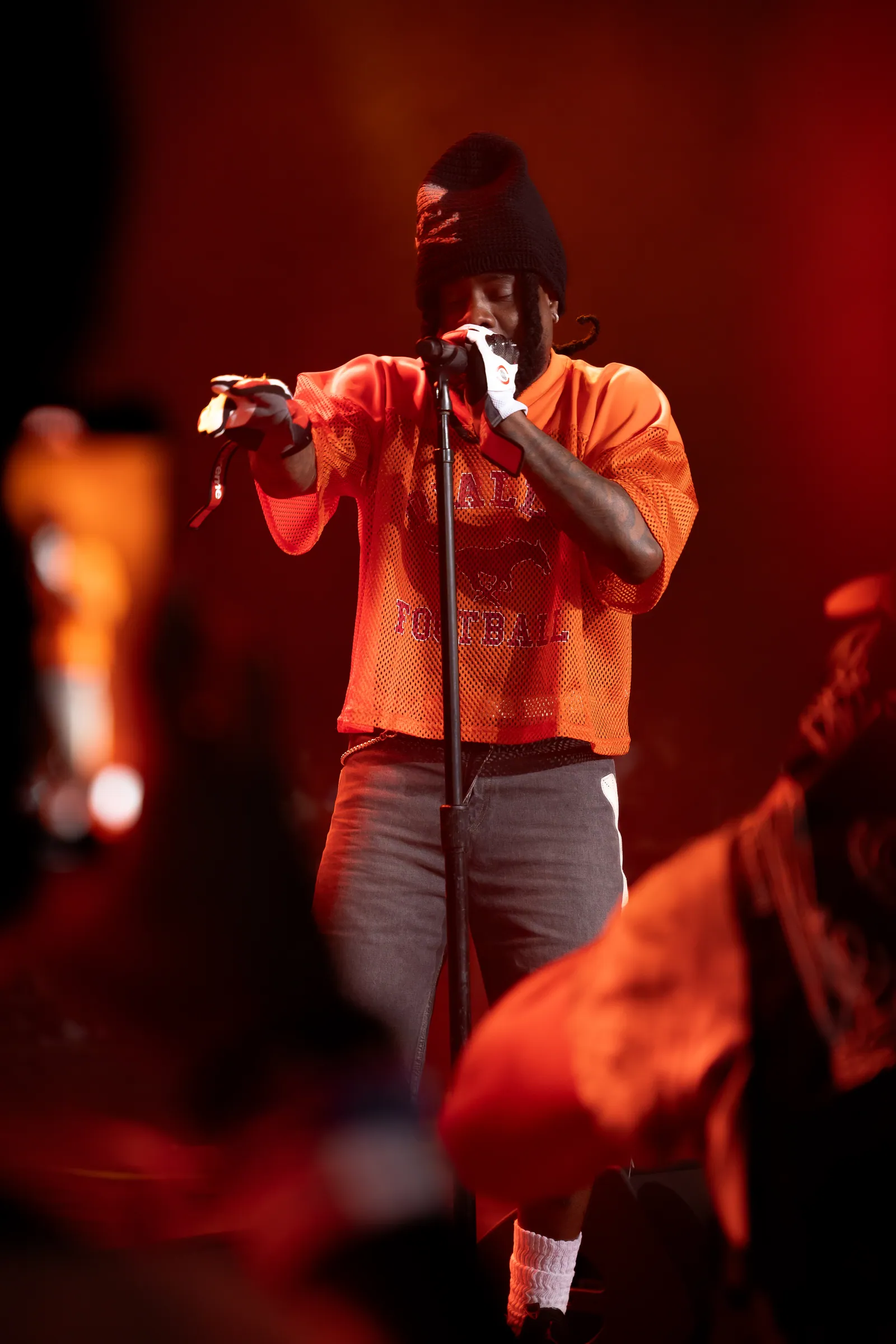 Wale performing on stage at Roots Picnic 2025 with a fan's camera phone visible in the foreground